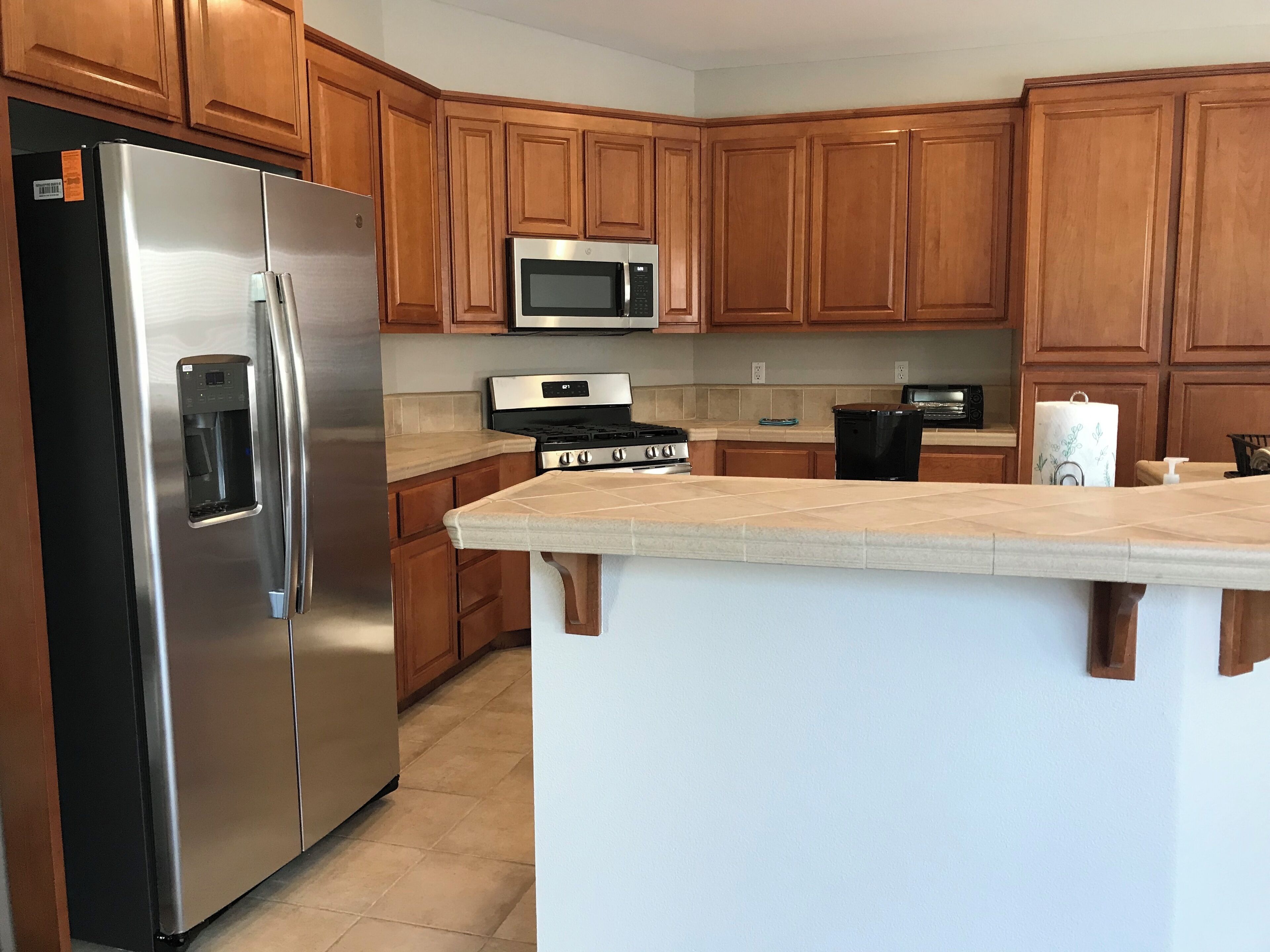A kitchen with wooden cabinets, a stainless steel refrigerator, a microwave, and a stove.