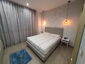 A modern bedroom with a large bed, a nightstand, a blue rug, and two wall-mounted lights.