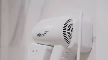 A white hair dryer mounted on a wall with a coiled cord.