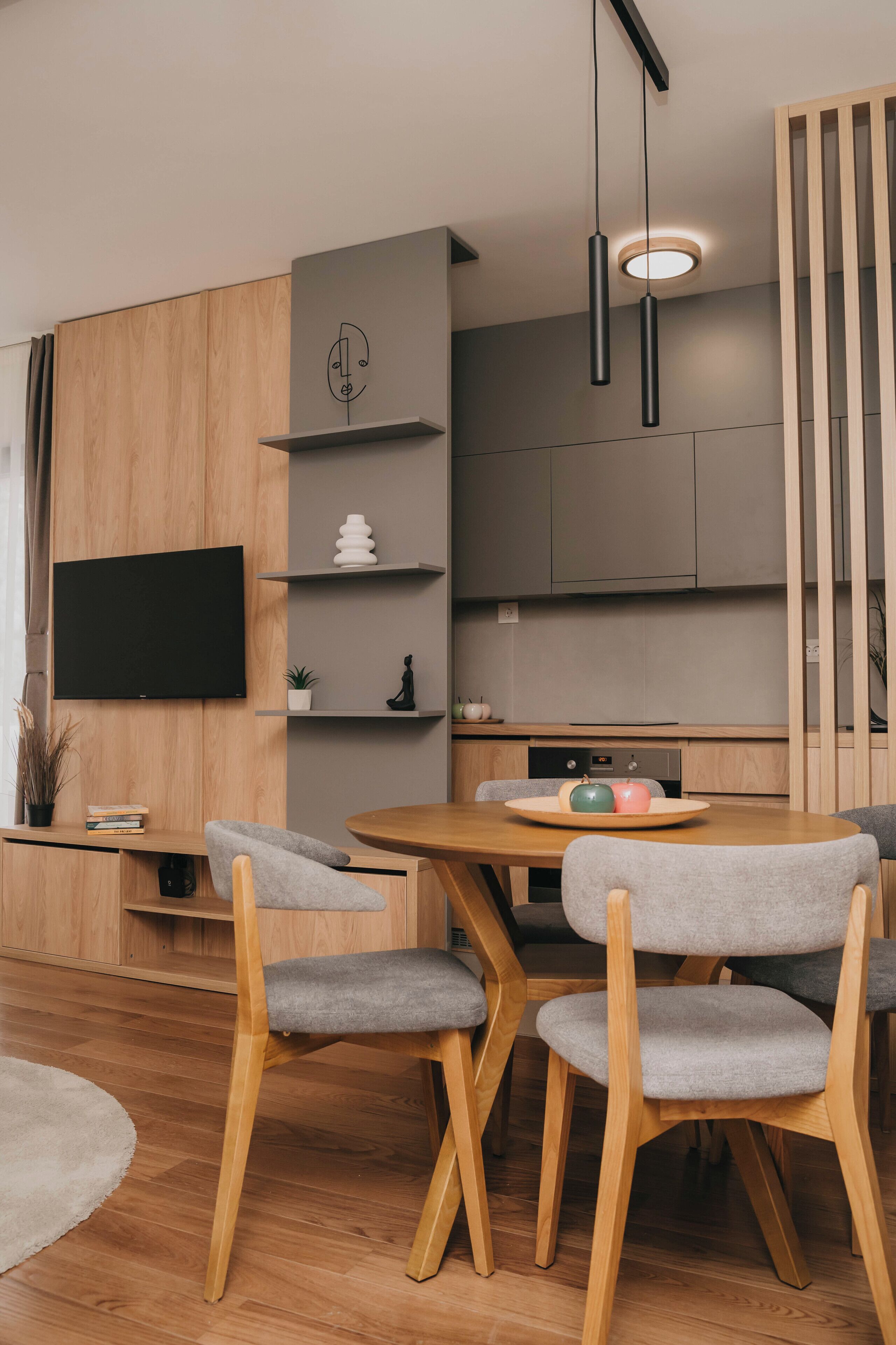 Ein moderner Essbereich mit einem Holztisch, grau gepolsterten Stühlen und einem an der Wand montierten Flachbildfernseher.