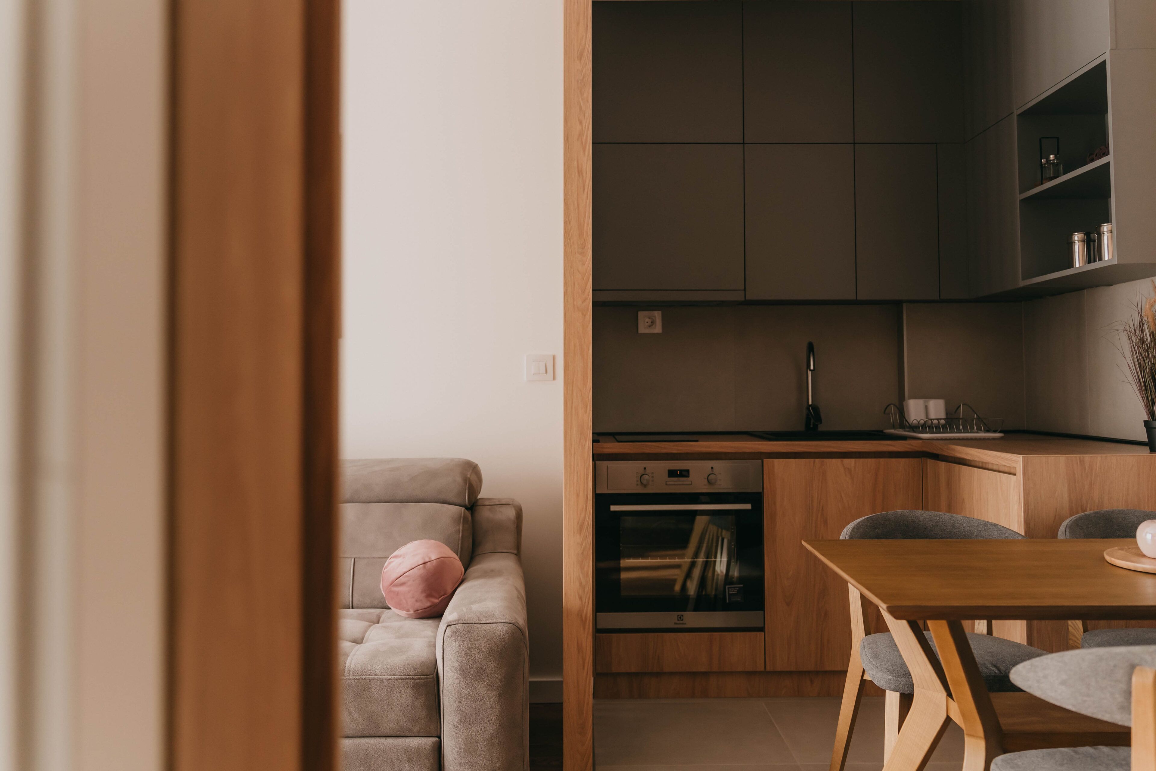 A modern kitchen with wooden cabinets, a built-in oven, and a dining area with a wooden table and chairs.