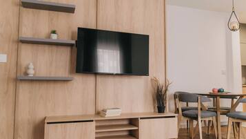 A modern living room with a flat-screen TV mounted on a wooden wall, a wooden console table with books, and a dining area with a table and chairs.