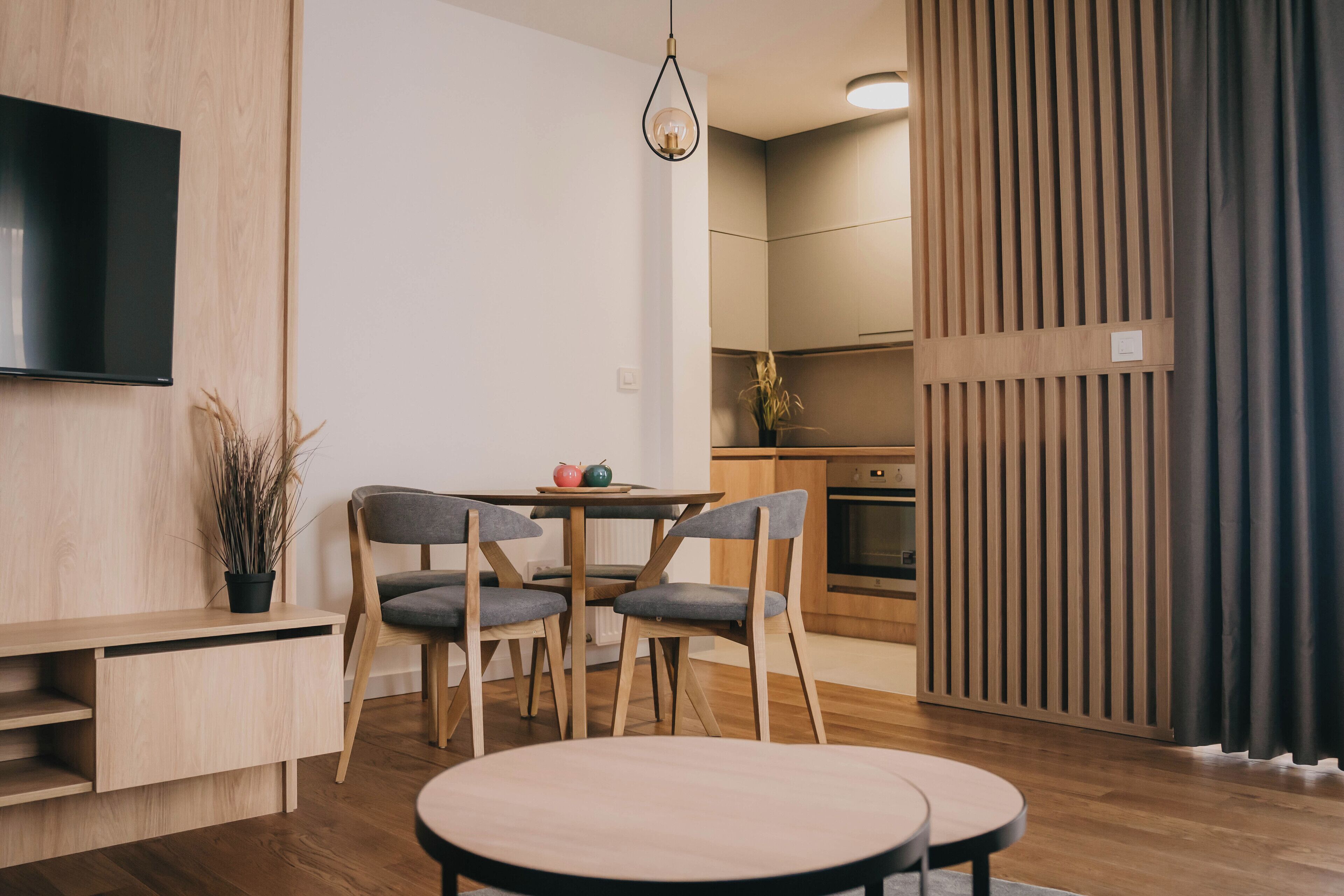 Una cocina moderna con armarios de madera, una mesa de comedor con sillas y un televisor de pantalla plana montado en la pared.