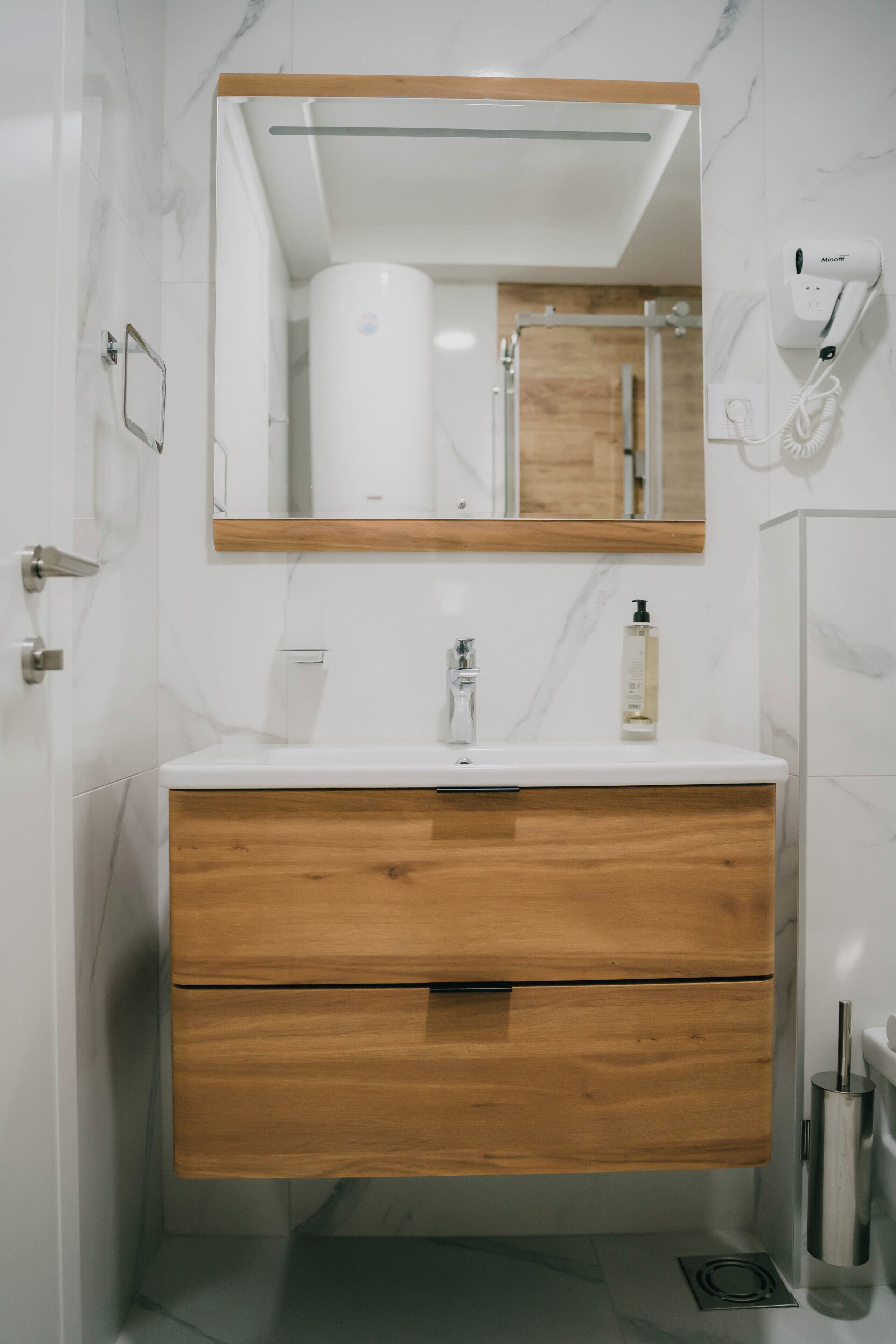 Un baño con lavamanos de mármol blanco, tocador de madera y un espejo encima.