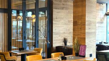 A modern restaurant interior with wooden flooring, yellow and green chairs, and pendant lighting.