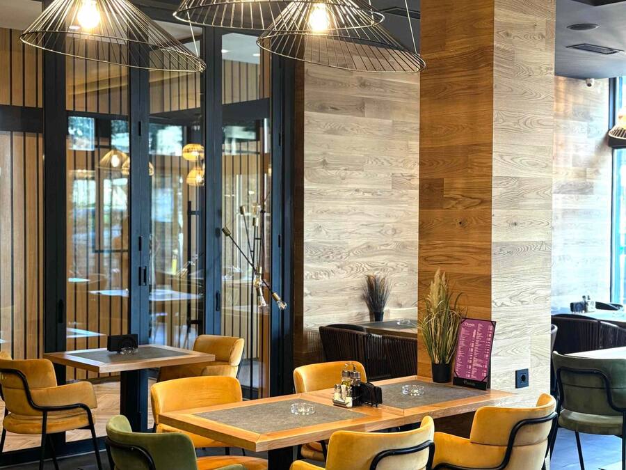 A modern restaurant interior with wooden flooring, yellow and green chairs, and pendant lighting.