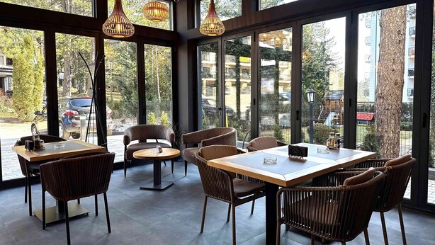 A restaurant with large windows, wicker chairs, and a wooden table. - Safran Zlatibor (Zlatibor)