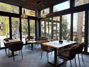 A restaurant with large windows, wicker chairs, and a wooden table. - Safran Zlatibor (Zlatibor)