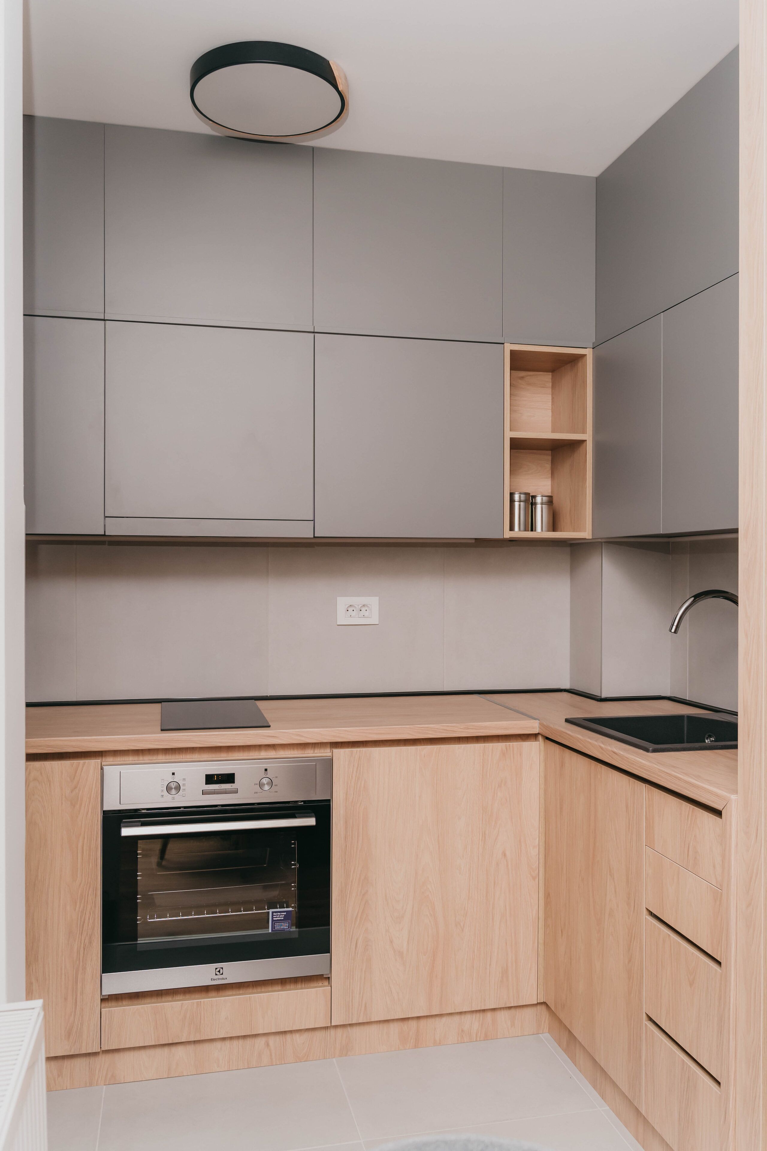 Una cocina moderna con armarios grises, encimera de madera, horno integrado y pileta de acero inoxidable.