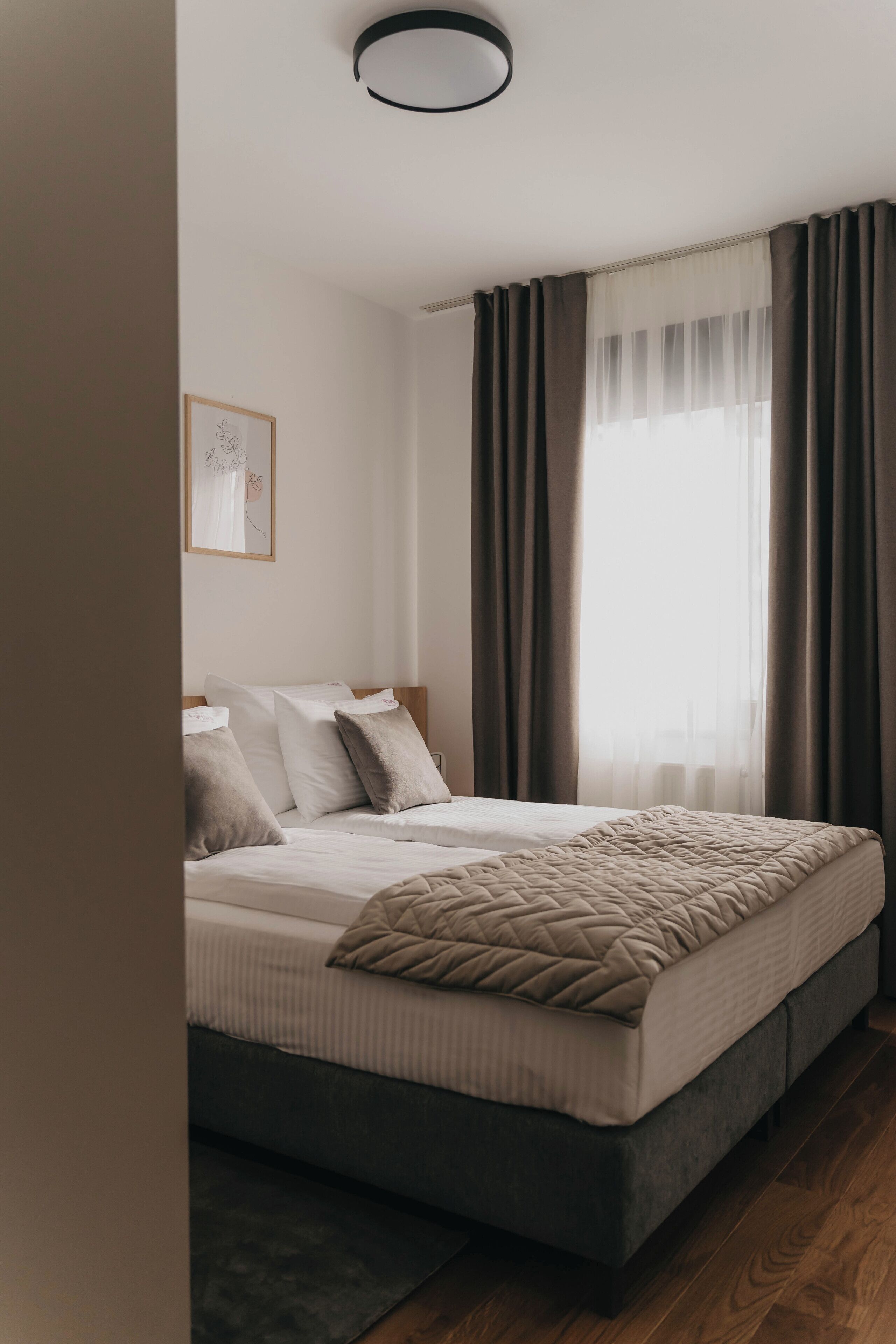 A modern bedroom with a large bed, a bedside table, a framed picture on the wall, and a window with curtains.