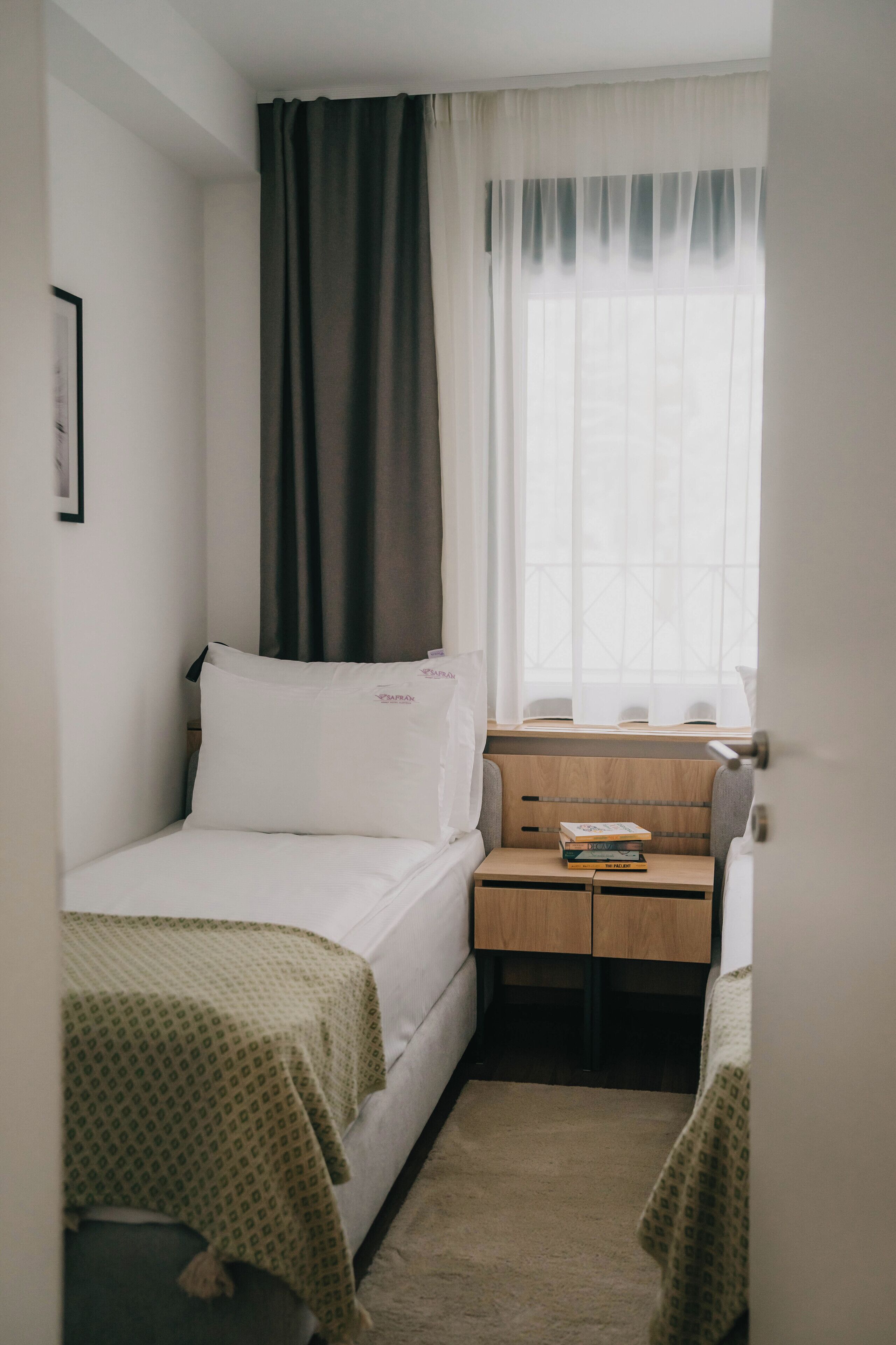 A small, neatly arranged room with a single bed, a desk with a chair, and a window with curtains.