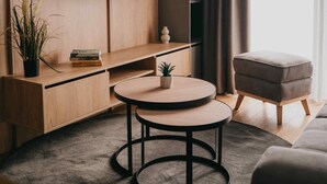 A modern living room with a round table, a flat-screen TV mounted on a wooden wall, a grey sofa, and a grey ottoman. - Safran Zlatibor (Zlatibor)