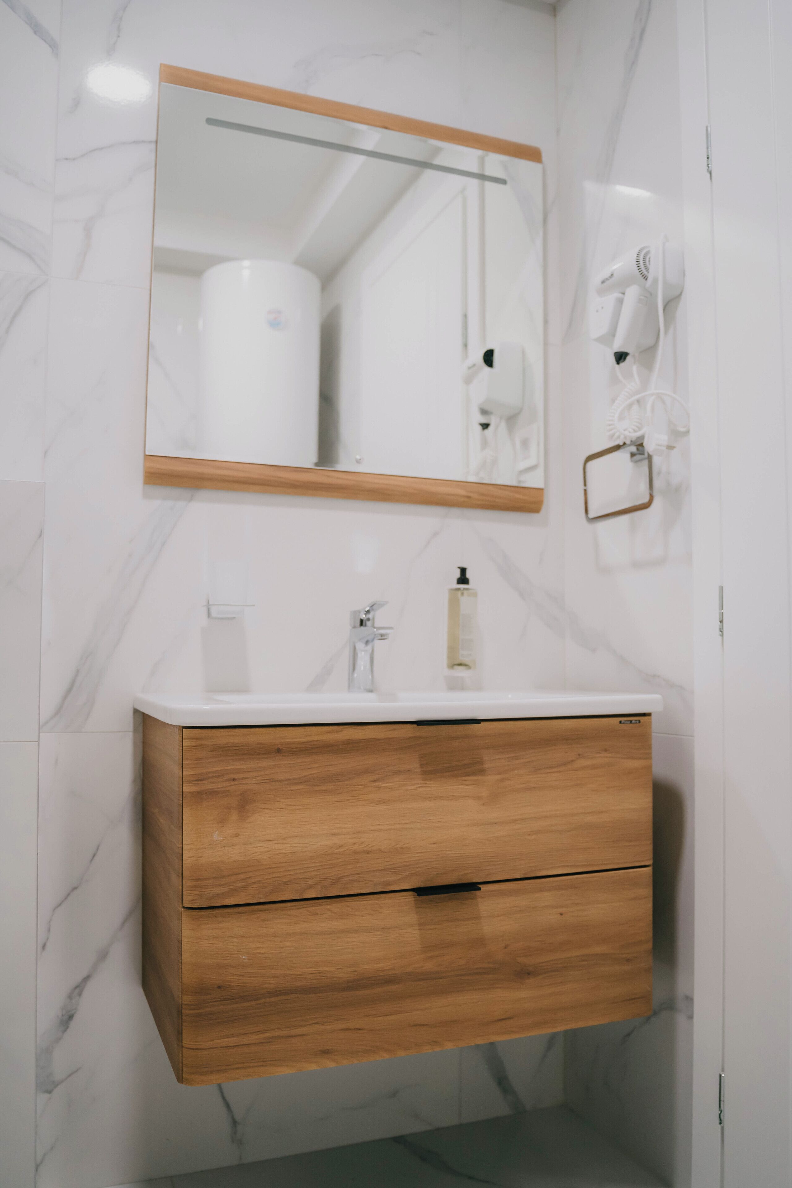 Un baño con pared de mármol, tocador de madera, espejo, toallero y secador de pelo.