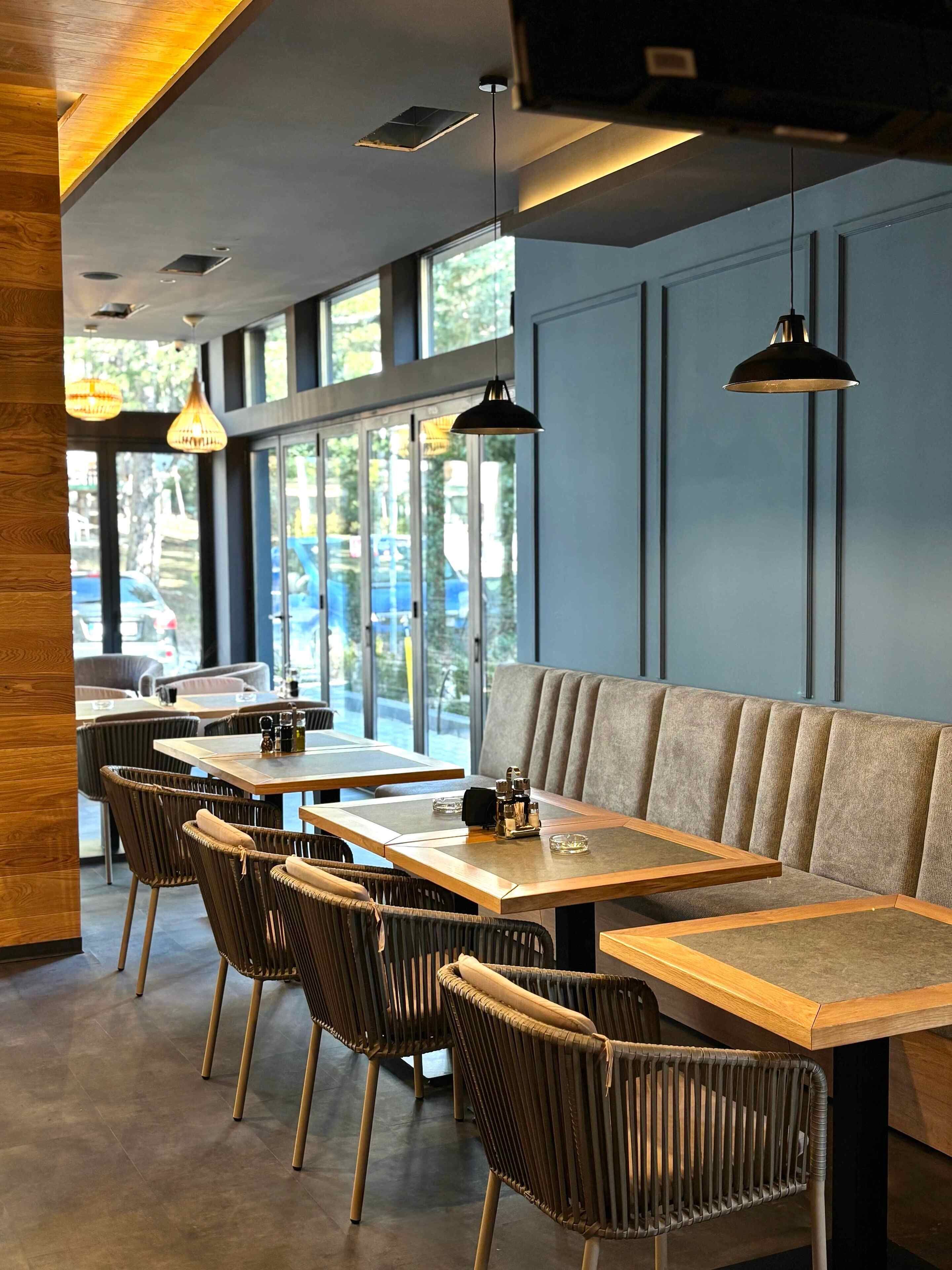 A modern restaurant interior with wooden tables, wicker chairs, and a grey upholstered bench.