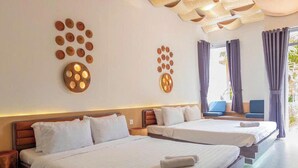 A hotel room with two beds, a wooden headboard, a wall art piece, and a window with curtains. - The Thousand Village (Mui Ne)