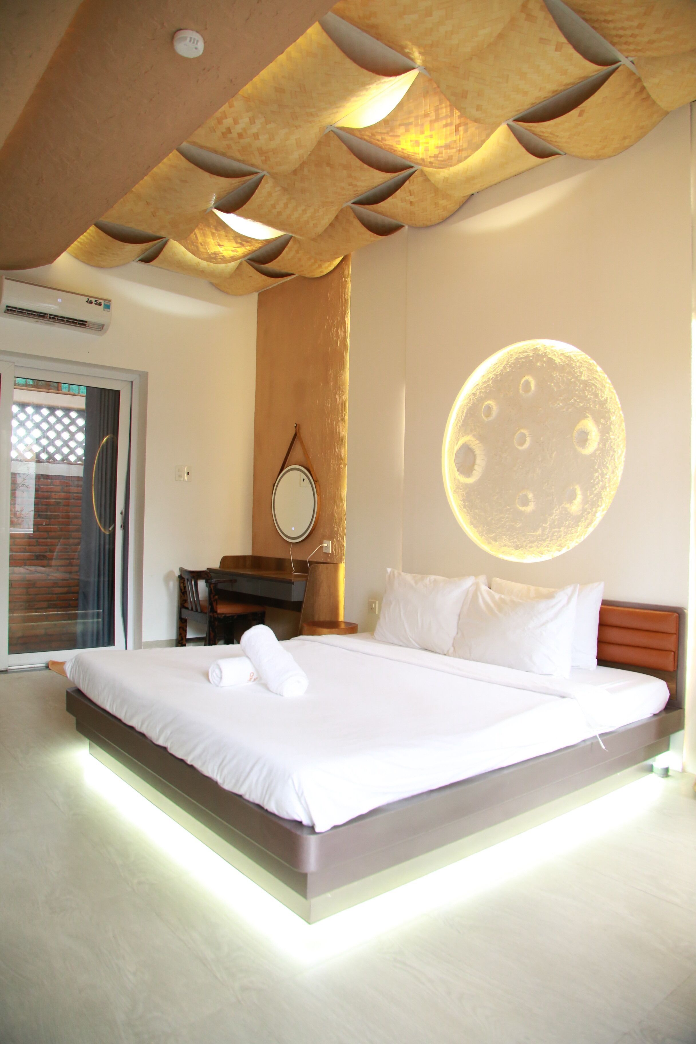Un dormitorio moderno con una cama grande, cabecera de madera, espejo montado en la pared y techo con un diseño geométrico único.