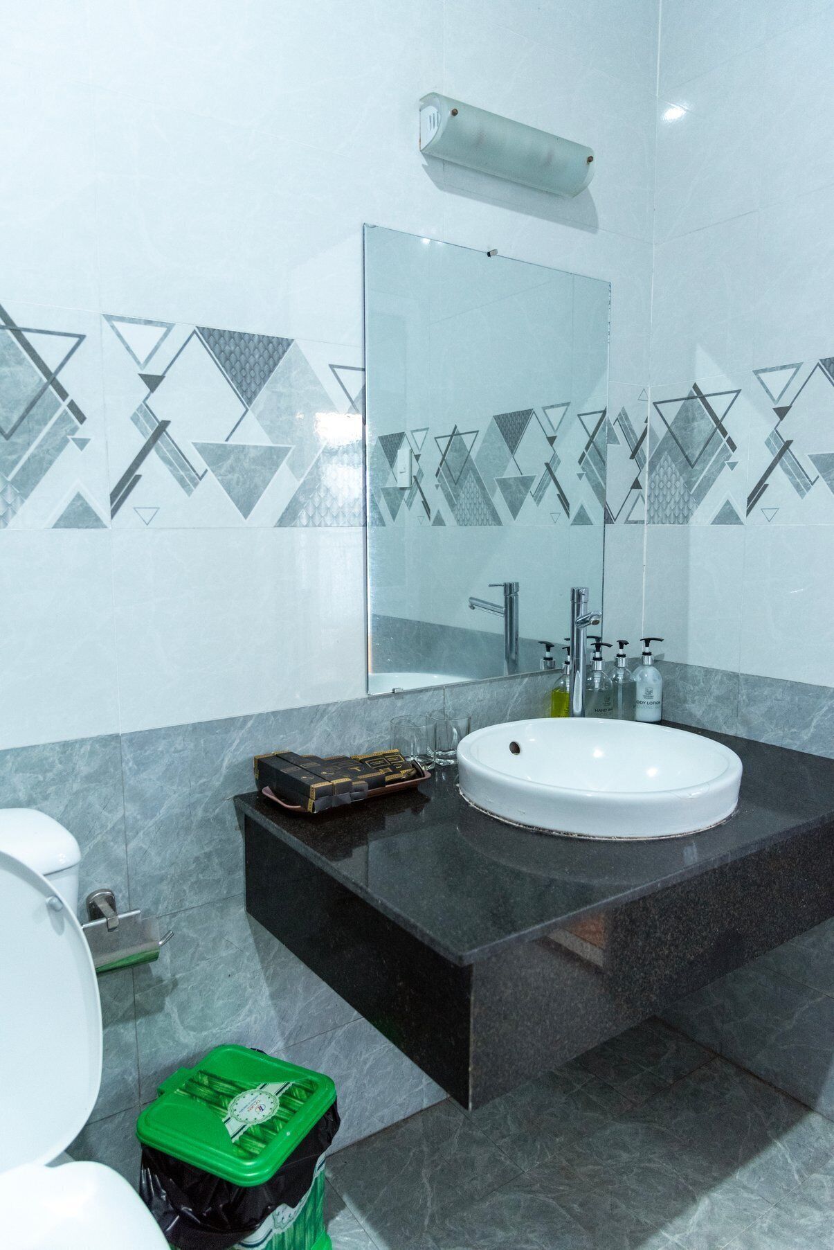 Un baño moderno con un lavamanos blanco, encimera oscura y baldosas con motivos geométricos.