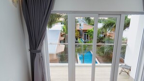 A room with a large sliding glass door leading to an outdoor area with a pool and greenery. - The Thousand Village (Mui Ne)