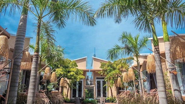 A pool surrounded by palm trees and a building with a modern design. - The Thousand Village (Mui Ne)