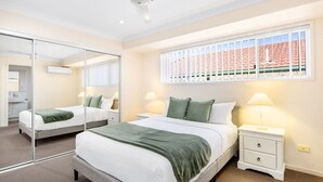 Une chambre à coucher avec un lit, des tables de chevet, un miroir et une fenêtre avec des stores.