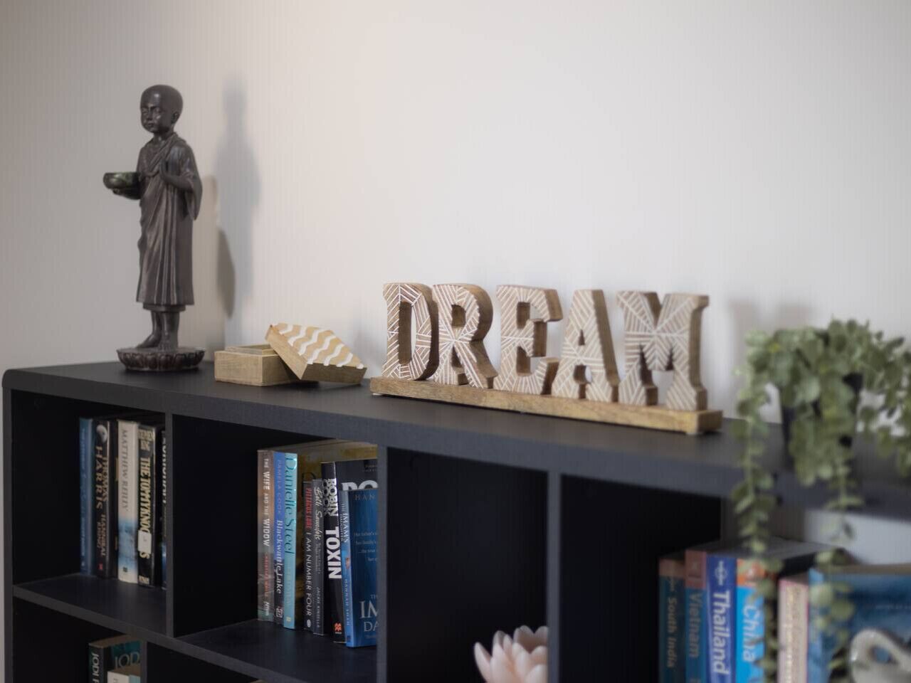 A bookshelf with books, a statue, and wooden letters spelling 'DREAM' on a wall.