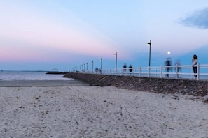 Une plage bordĂ©e dâune clĂŽture blanche, dâun mur de pierre et dâune jetĂ©e qui sâavance dans lâeau.
