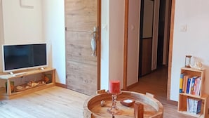A living room with a wooden TV stand, a red candle on a wooden barrel, a bookshelf, and a wooden door. - Cottage "Les Cannas" with swimming pool (Arès)