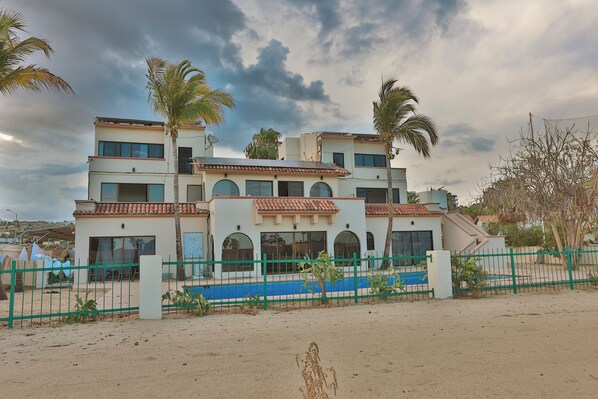A multi-story building with a flat roof, large windows, and a blue swimming pool in the foreground.