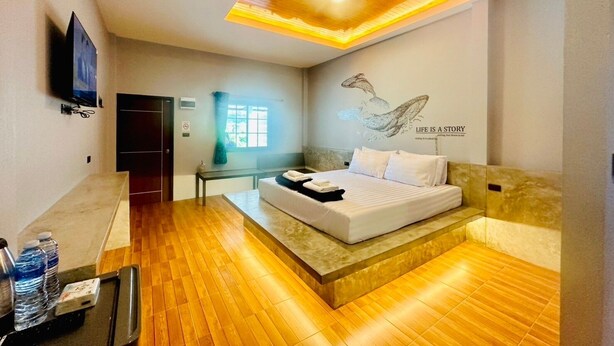 Une chambre d’hôtel moderne avec un plancher en bois, un lit recouvert de draps blancs, un téléviseur fixé au mur et une œuvre d’art décorative.