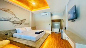 Une chambre d’hôtel moderne dotée d’un grand lit, d’un plafond en bois, d’un téléviseur fixé au mur et d’une salle de bain visible à travers une porte ouverte.