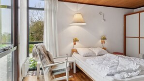 Ein Schlafzimmer mit großem Fenster, einem Bett, einem Sessel und zwei Wandlampen.