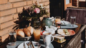 Una mesa de desayuno con diversos alimentos, un jarrón con flores y una ventana con persianas.