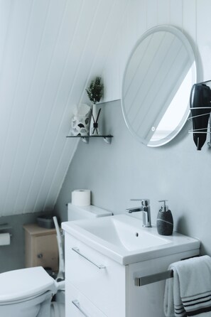 Ein modernes Badezimmer mit einem weißen Waschbecken, einem runden Spiegel und einem Handtuchhalter.