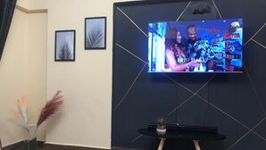Ein modernes Wohnzimmer mit einem Flachbildfernseher an einer dunklen Wand, einem kleinen schwarzen Tisch mit einer Pflanze und zwei gerahmten Bildern.