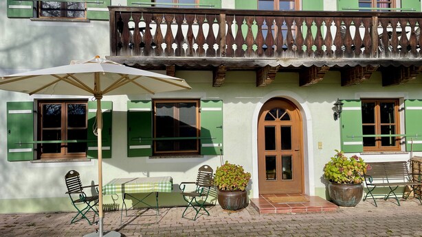 Un edificio tradicional con balcón, mobiliario exterior y plantas en macetas.