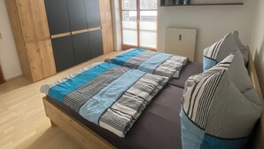 A bedroom with a bed, a wardrobe, a radiator, a window, and a shelf with books. - Vacation apartment for 2 persons, 50 m², 1 separate bedroom, balcony (Inzell)