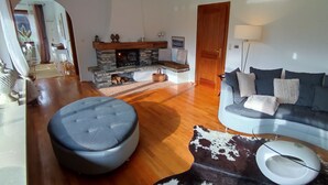 A living room with a stone fireplace, a sofa, a round ottoman, and a cowhide rug. - Vacation home Harmony 2 to 6 persons (Übersee)