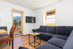 Een moderne woonkamer met een bank, een bijzettafeltje en een aan de muur bevestigde televisie.
