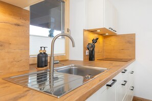 Una cocina moderna con pileta de acero inoxidable, encimera de madera y alacenas blancas.