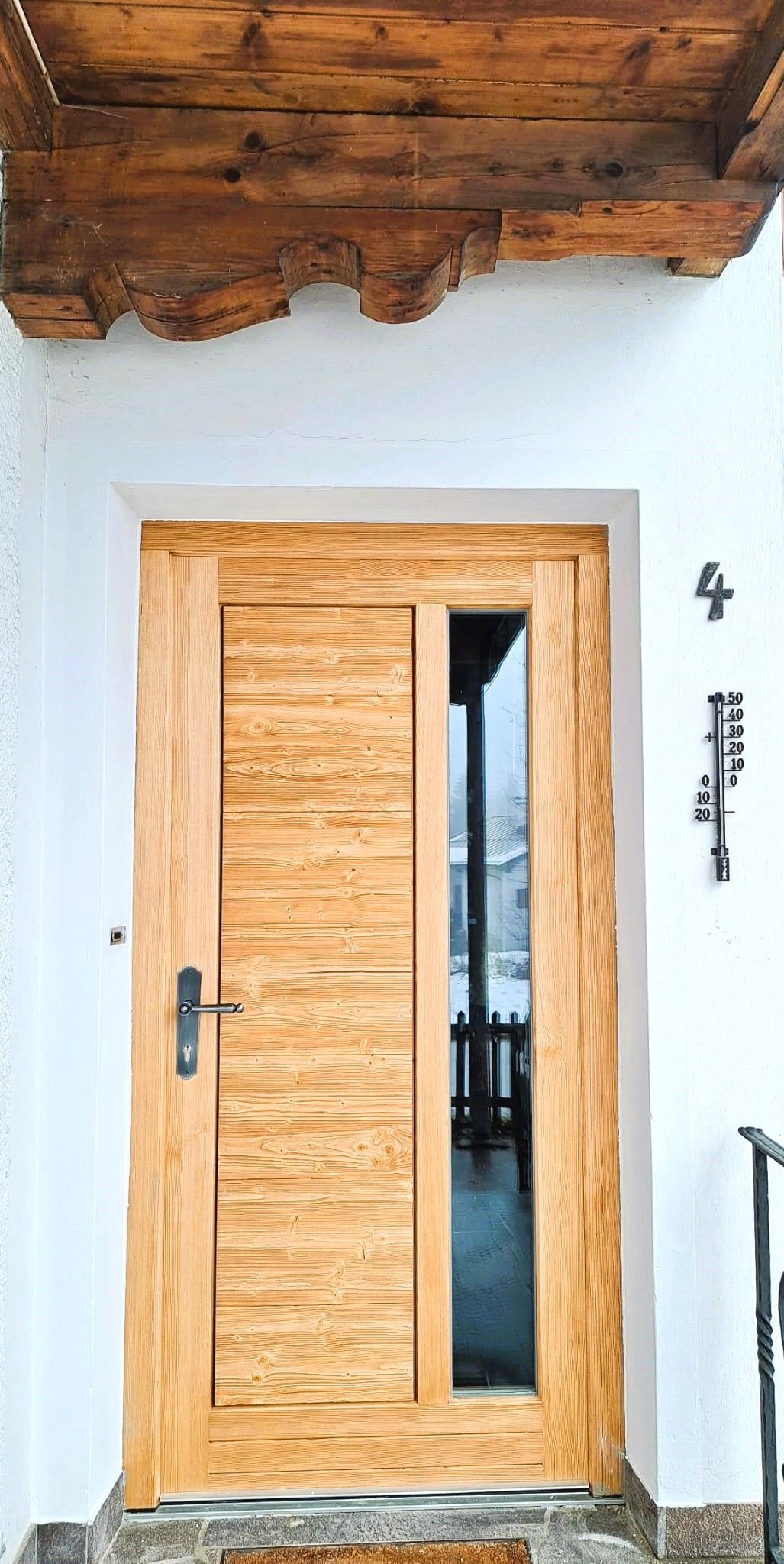 A wooden door with a glass panel, a metal door handle, and a small metal plaque with the number '4' on the wall.