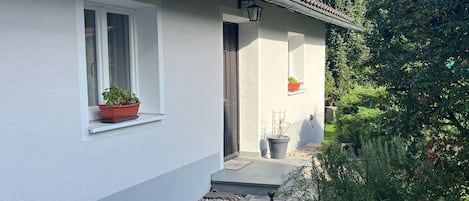 Ein Haus mit weißer Fassade, einem Ziegeldach und einer kleinen Veranda mit Topfpflanzen.