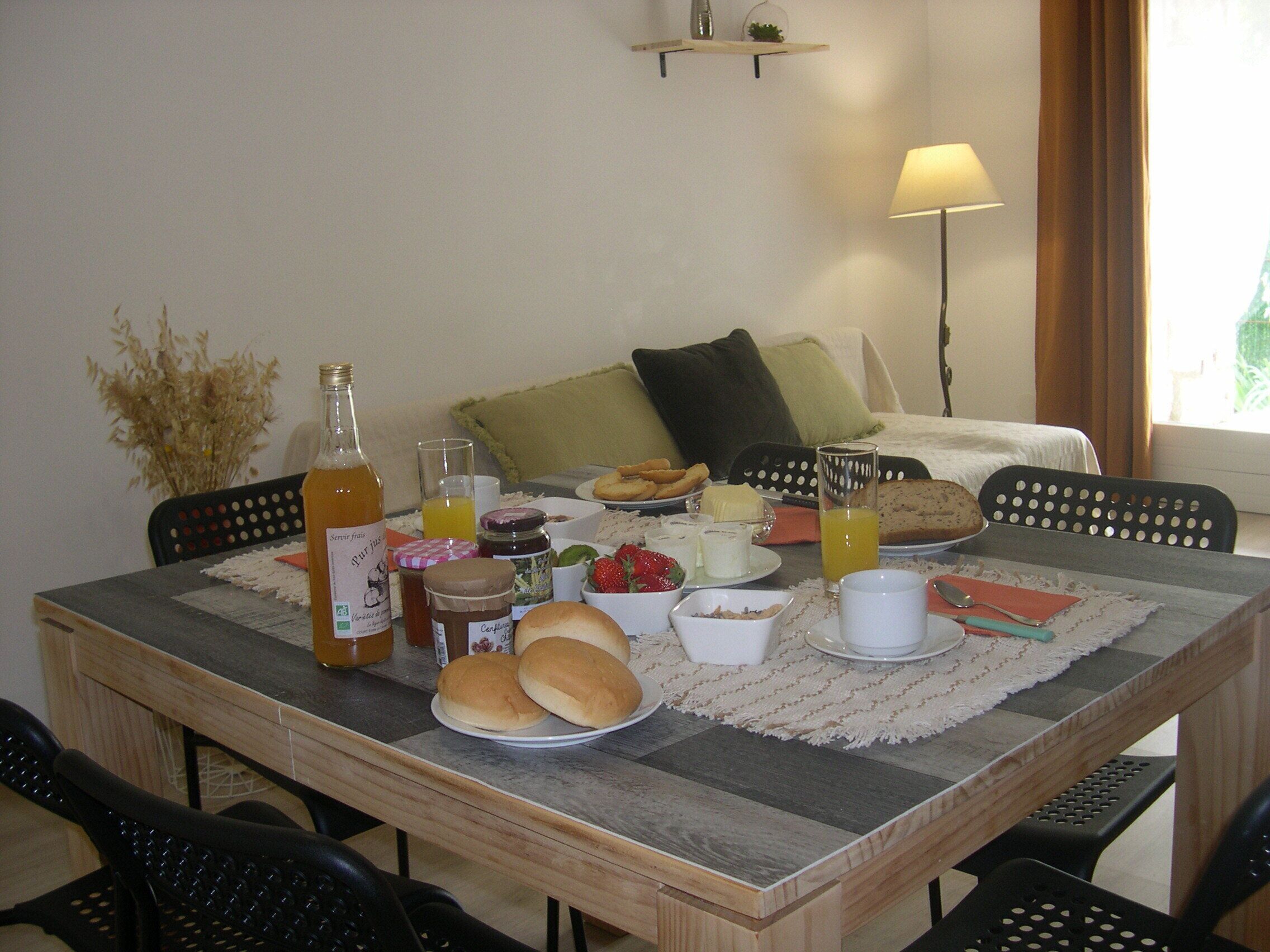Una mesa de desayuno con diversos alimentos, una botella y un vaso de zumo de naranja.