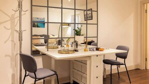 A dining area with a white table, two chairs, a decorative mirror, and a coat rack.