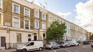 A row of terraced houses with a tree in the middle, parked cars, and a clear sky.