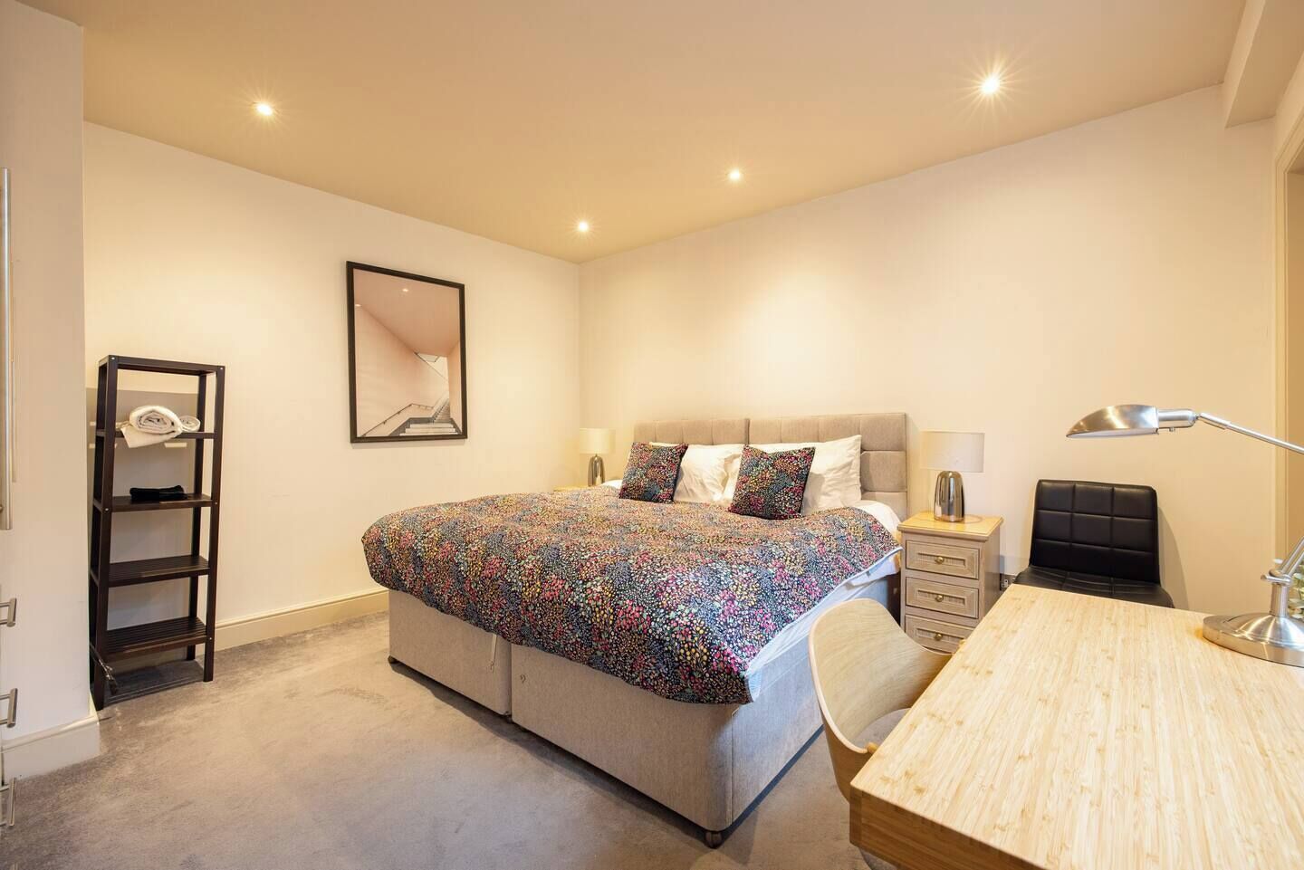 Un dormitorio con cama, mesita de noche, lámpara, silla y un escritorio pequeño.