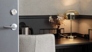 Una cocina moderna con encimera oscura, hervidor de acero inoxidable, un jarrón con flores secas y una lámpara de mesa.