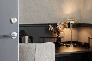 A modern kitchen with a dark countertop, a stainless steel kettle, a vase with dried flowers, and a table lamp. - Centralhotellet Tierp (Tierp)