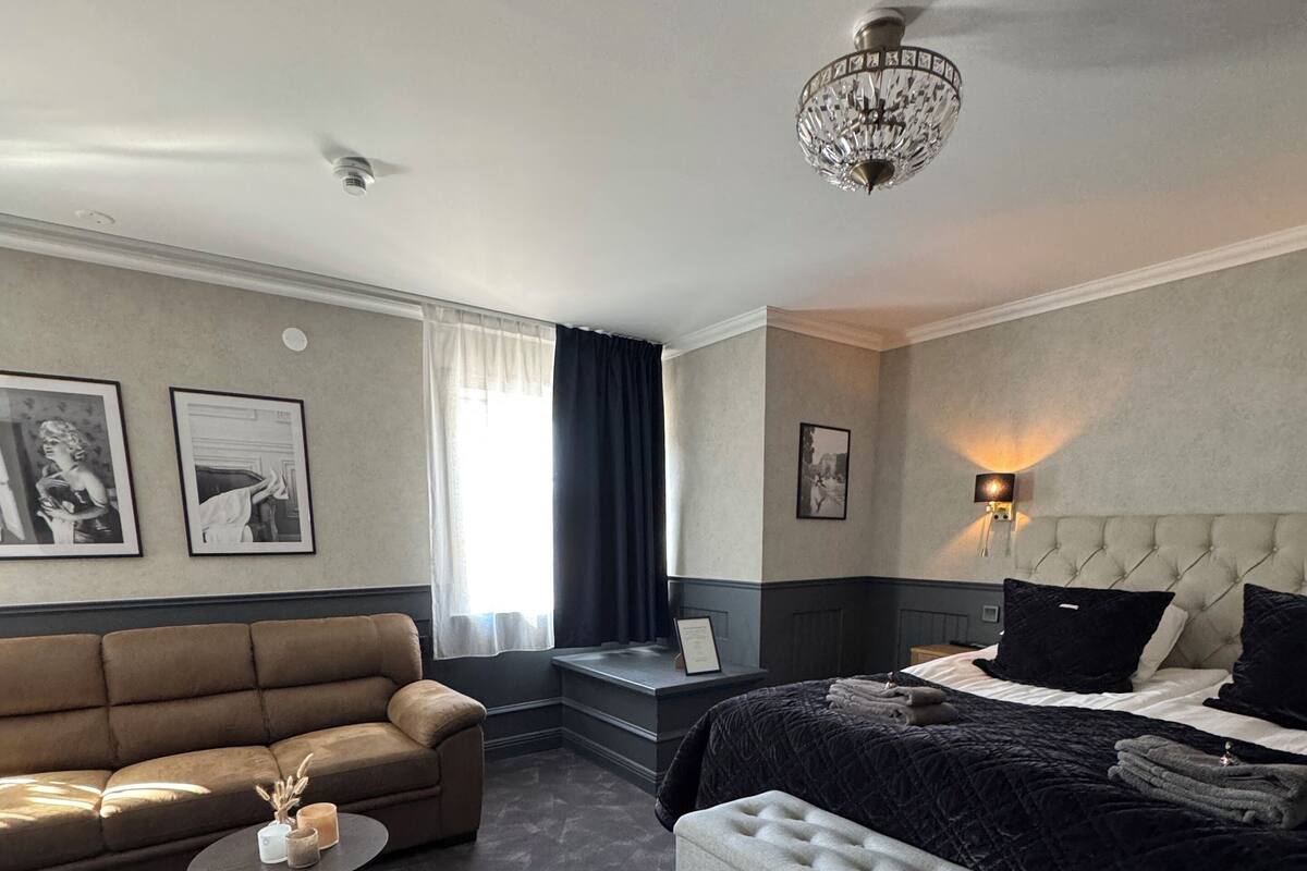 A hotel room with a bed, a sofa, a small table, and a chandelier.