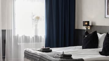 A bedroom with a large bed, a chandelier, a nightstand, and a window with curtains.