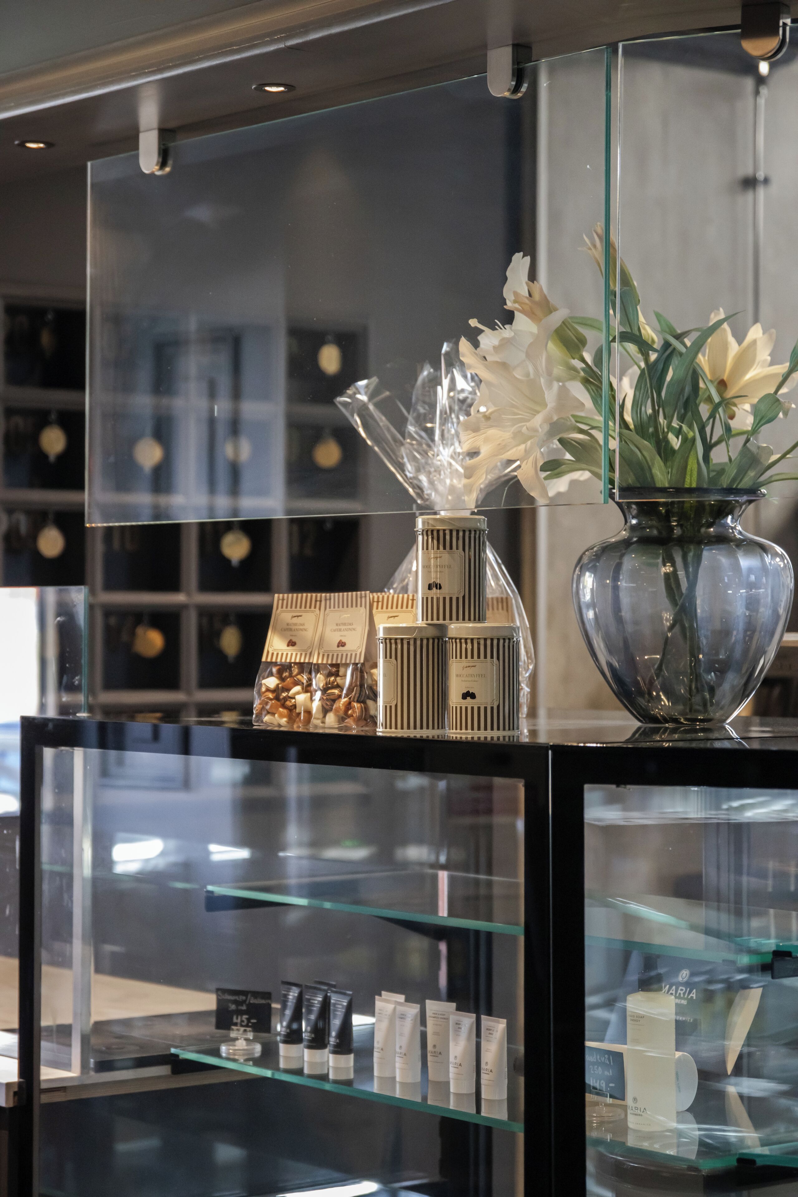 A display counter with a glass vase of flowers, a model house, and various packaged items.